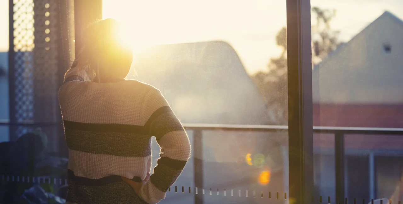 Woman watching sunset from home. Photo: iStock /